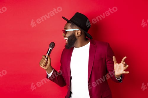Preview: Passionate black male singer performing against red background, singing into microphone, wearing