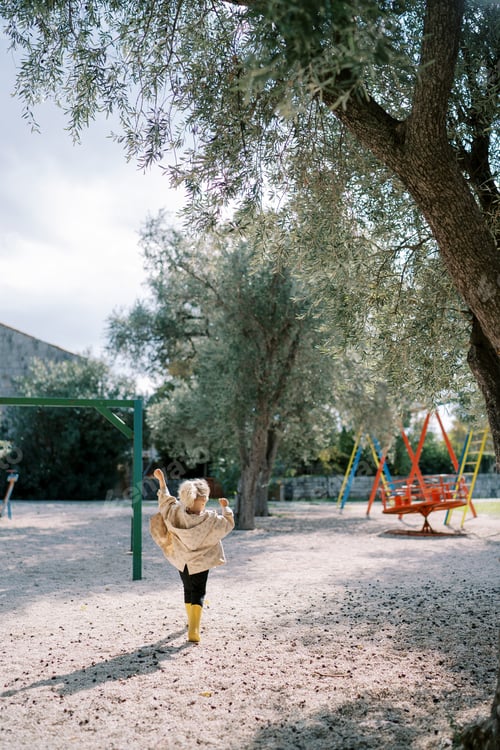 Preview: Little girl walks along the playground towards a colorful carousel. Back view