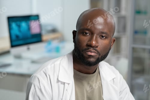 Preview: Portrait of serious scientist or chemist in lab coat sitting in front of camera