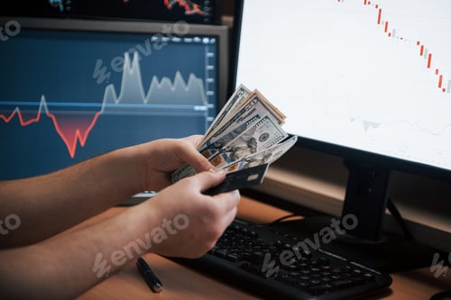 Preview: human hands holds money in the office with multiple screens with graphs