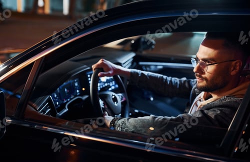 Preview: Side view of handsome unshaved man in fashionable clothes that riding his automobile