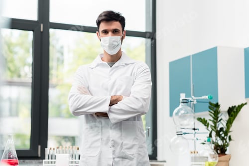 Preview: Confident professional scientist in protective mask and lab coat standing with crossed arms and