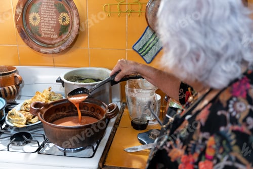 Preview: A senior mexican woman is preparing red chili sauce using a gas stove. Close up