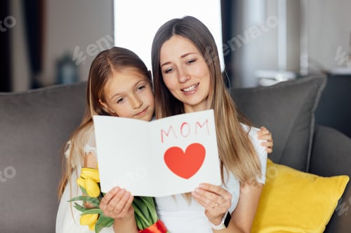 Preview: Happy caucasian mommy and daughter sitting on couch and celebrating mother's day at home