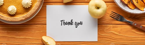Preview: top view of delicious pumpkin pie, apples and thank you card on wooden orange table, panoramic shot