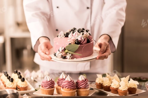 Preview: partial view of confectioner holding cake in hands in restaurant kitchen