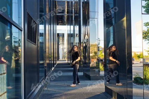 Preview: Young happy woman with dreadlocks in park. Modern building on background.