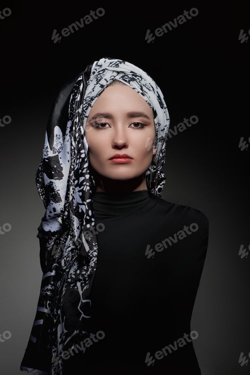 Preview: Woman poses in black clothing with a patterned headscarf in a dark setting