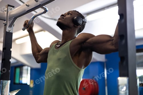 Preview: Muscular athlete executing pull-ups, wearing headphones during strength training workout