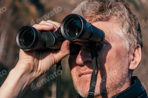 Preview: Portrait of a middle-aged man looking through binoculars. Close-up.