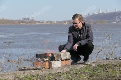 Preview: A man sits by the fire on the beyereg of the river.