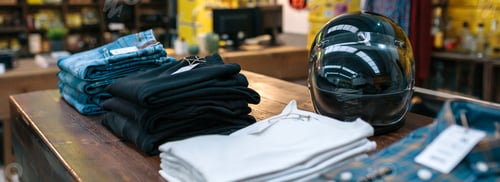 Preview: Black motorbike helmet and new clothes collection over counter on vintage store