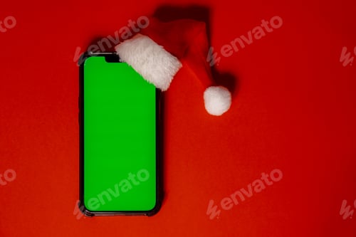 Preview: Mobile phone dressed in Santa-Claus red-white hat with chroma key screen against red background
