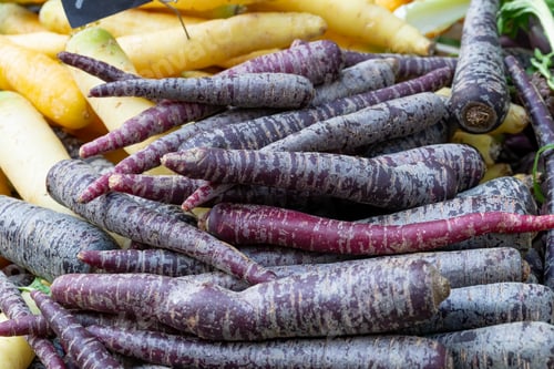 Preview: Pile of purple carrots on a market stall.