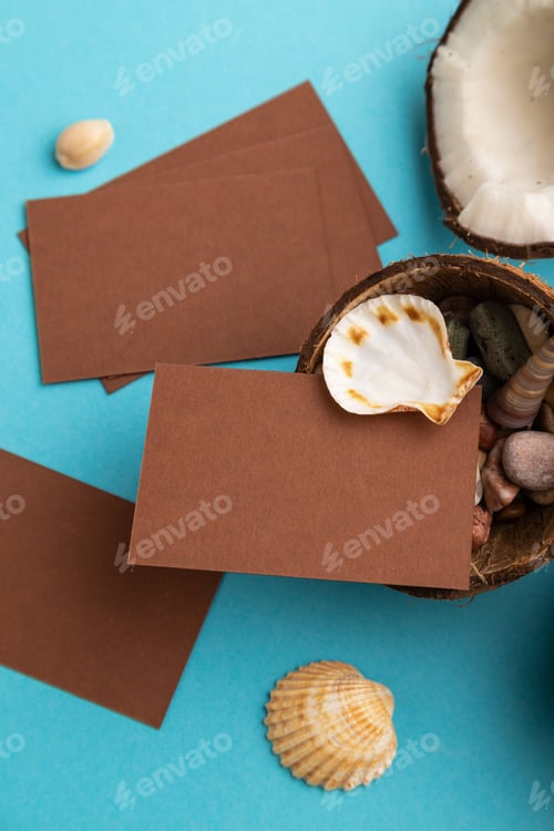 Preview: Brown paper business card with coconut and seashells on blue pastel background. Top view