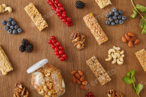 Preview: Top view of food composition of berries, nuts, cereal bars, mint and jar of granola on wooden