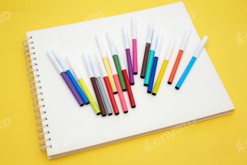 Preview: Set of colorful felt-tip pens on a notepad on a yellow table