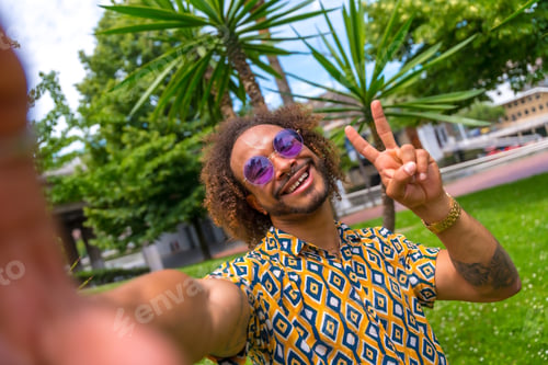 Preview: Afro-haired man on summer vacation next to some palm trees by the beach taking a selfie