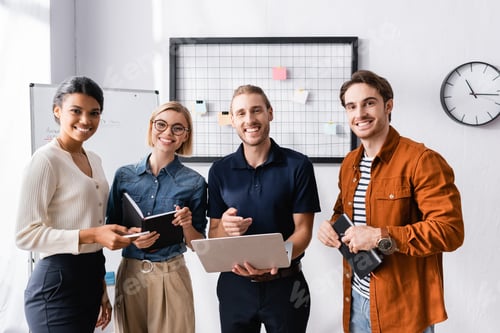 Preview: happy businessman pointing at laptop near happy multicultural colleagues
