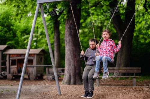 Preview: Little junior girl in spring outfit rides on swings with big man with dark long hair in glasses