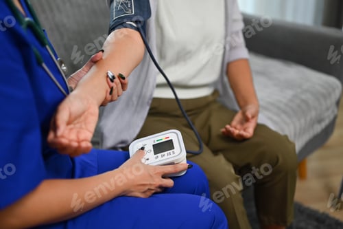 Preview: Healthcare worker measuring blood pressure senior woman during home visit.