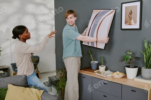 Preview: Black Woman Guiding Man Hanging Wall Art in Home Interior