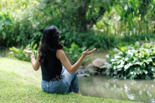 Preview: Woman meditating in lush green park by the river, embracing nature's serenity