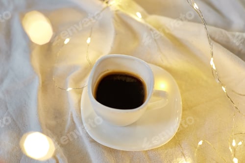 Preview: Cup of coffee in bed with a gerlands lights, copy space.