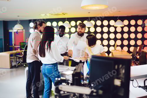 Preview: Diverse male and female colleagues discussing information near table desktop with documents