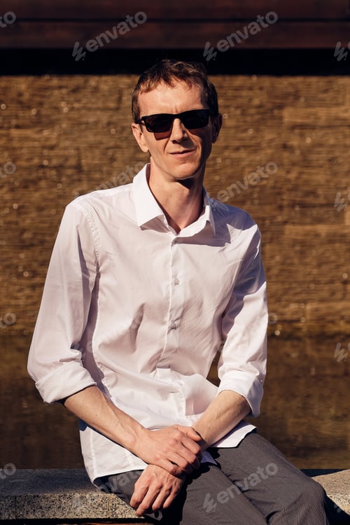 Preview: Middle age man in sunglasses sitting in shade in hot sunny day