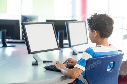 Preview: Boy typing on keyboard at round table in school computer lab among three monitors, copy space