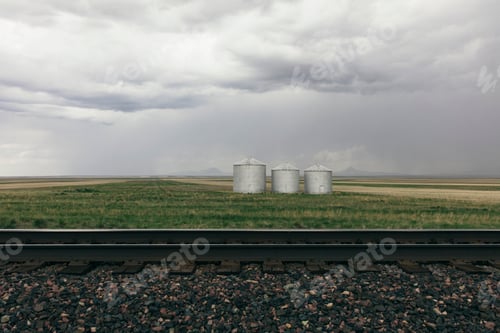 Preview: Grain silos and storm clouds over vast farmland and prairie, train tracks in foreground