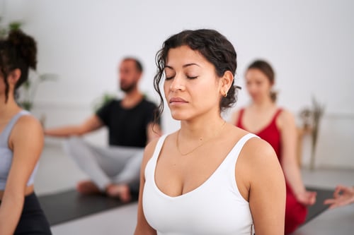 Joven latina de cerca con los ojos cerrados practicando ejercicios de yoga en interiores. Grupo de personas