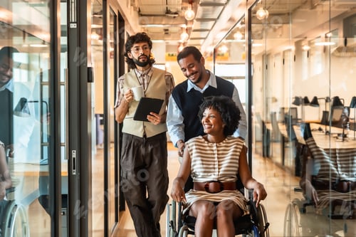 Preview: Diverse business colleagues pushing woman in wheelchair at office