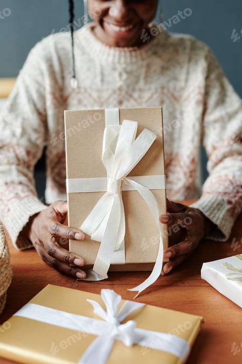 Preview: Young woman opening giftbox by table