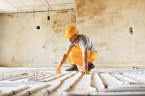 Preview: Worker in yellow colored uniform installing underfloor heating system