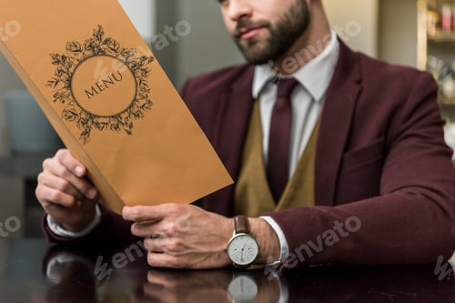 Preview: cropped view of businessman in formal wear sitting at restaurant and holding menu