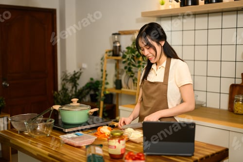Preview: Smiling asian woman preparing ingredients for spaghetti on a wooden counter