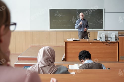 Preview: Mature man standing by blackboard during explanation of subject