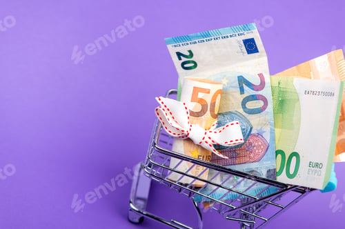 Preview: roll of euro banknotes with white ribbon in supermarket trolley cart isolated on purple background