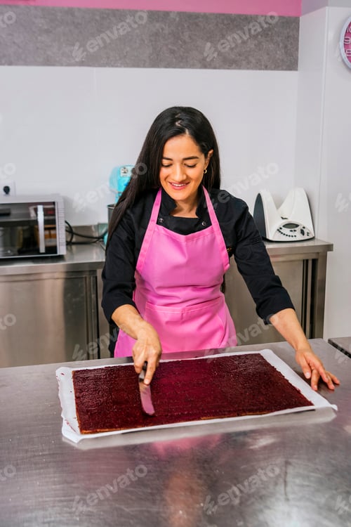 Preview: Colombian pastry chef smiling spreads berry jam on the cake