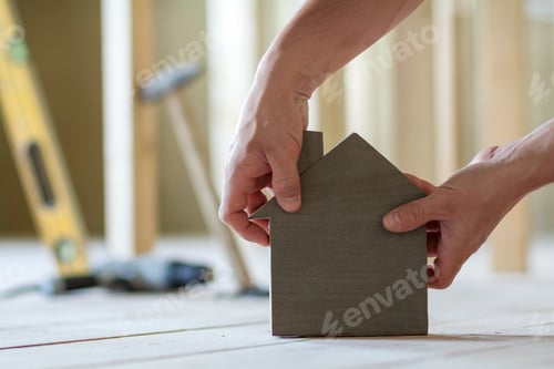 Preview: Close-up of muscular male hands holding small brown wooden model house