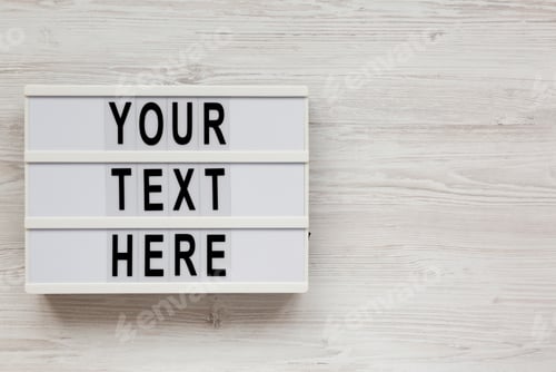 Preview: 'Your text here' words on a modern board on a white wooden background, top view.