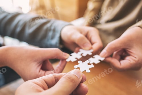 Preview: Closeup image of people's hands holding and putting a piece of white jigsaw puzzle together