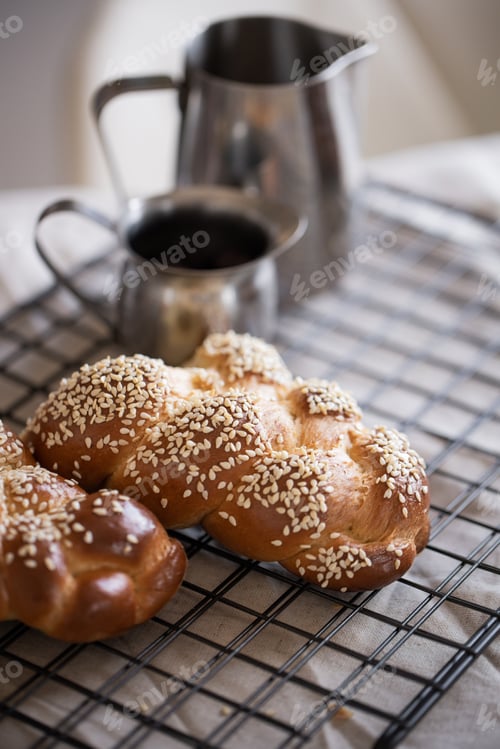 Preview: Fresh challah with sesame seeds on a baking rack with tin containers in the background