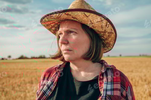 Preview: Portrait of female farmer wearing straw hat standing in ripe wheat field and thinking