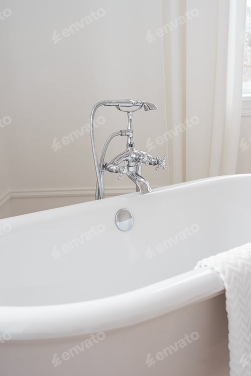 Preview: Shiny metal chrome faucet, elegant water tap on white freestanding bathtub in bathroom