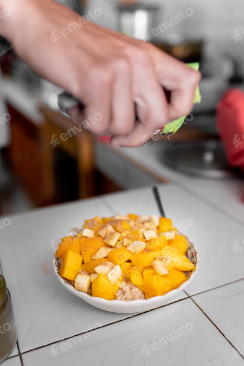Preview: An unrecognizable young man is pouring cinnamon on top of his porridge with mangos, bananas and oats