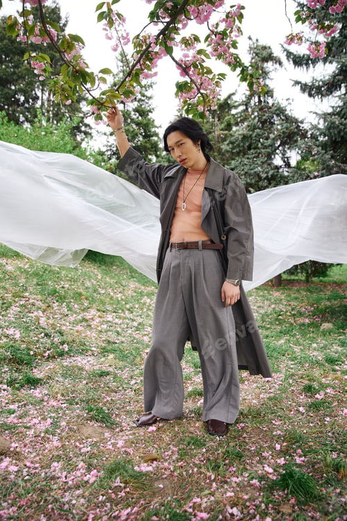 Preview: Stylish young man enjoys a tranquil day in a lush park surrounded by blossoming trees