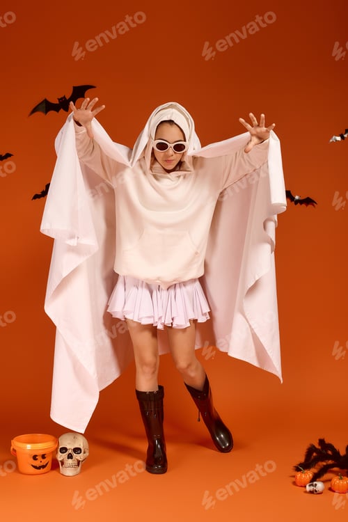 Preview: Cute girl in Halloween attire celebrates spooky season against bright orange backdrop